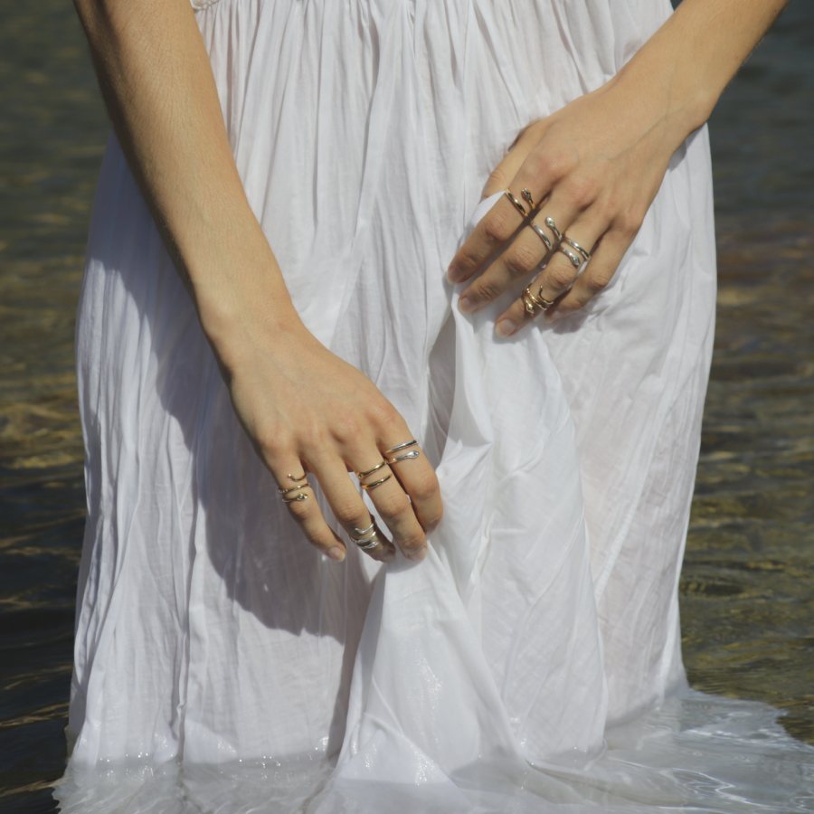 Model wearing a white dress with multiple handmade snake rings by Izaskun Zabala, standing in water.