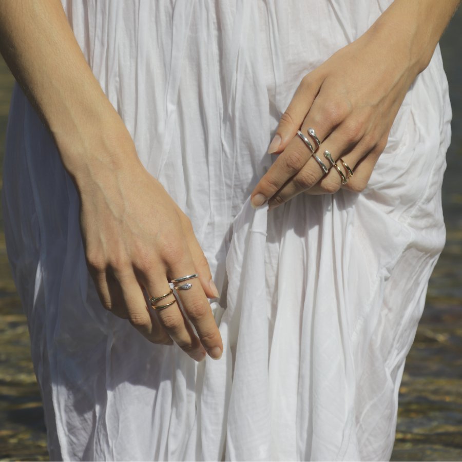 Close-up of hands with multiple snake rings handmade by Izaskun Zabala, on a natural background.