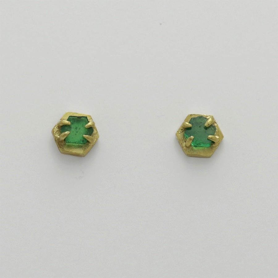Pair of green emerald stud earrings with golden hexagonal settings on a light gray background, handmade by Izaskun Zabala.
