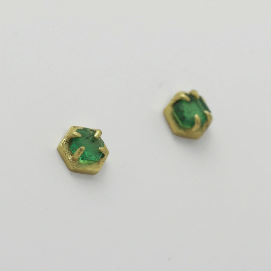 Pair of green emerald stud earrings with golden hexagonal settings on a light gray background, handmade by Izaskun Zabala.