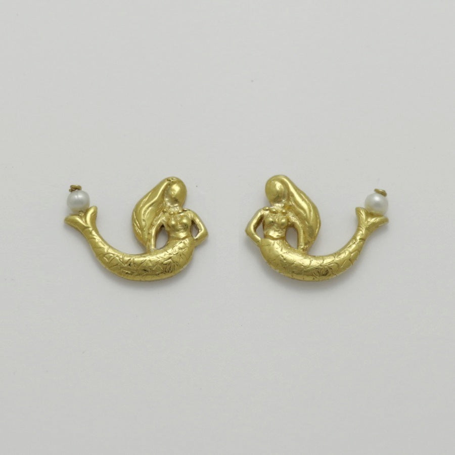 Golden mermaid-shaped earrings with freshwater pearls on a light gray background, handamade by Izaskun Zabala.