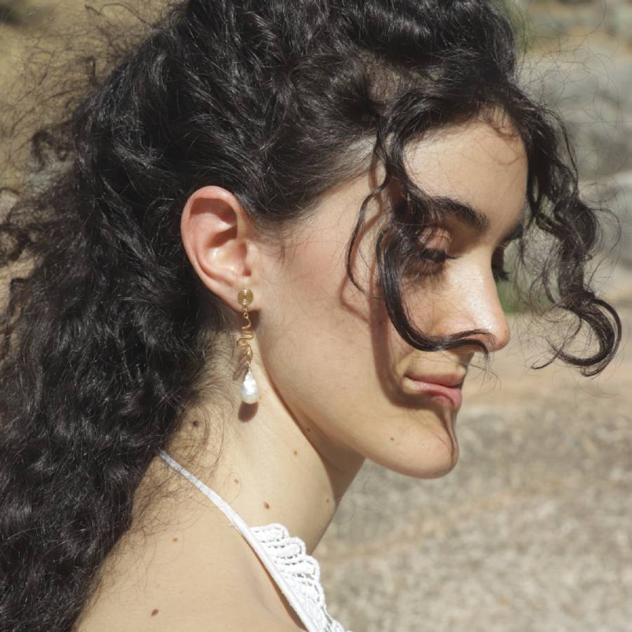 Woman with long dark hair wearing gold snake earrings with a baroque pearl drop, handmade by Izaskun Zabala.