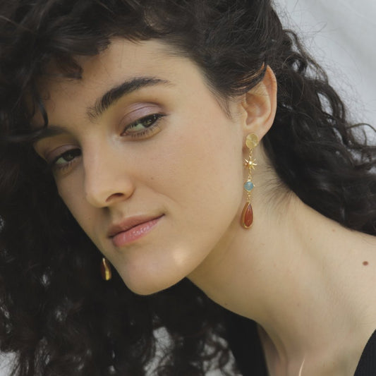 Image is a pair of 24K gold plated drop earrings with spiral stud, celestial motifs, chalcedony and carnelian gemstones on model, handmade by Izaskun Zabala.