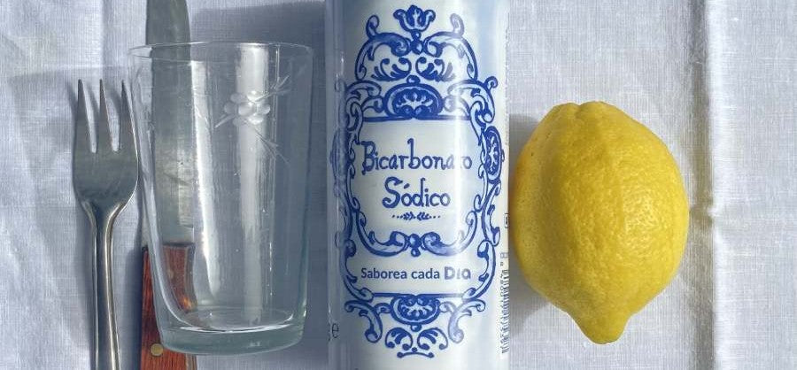 Bicarbonate soda can, lemon, glass, and fork on a white cloth background