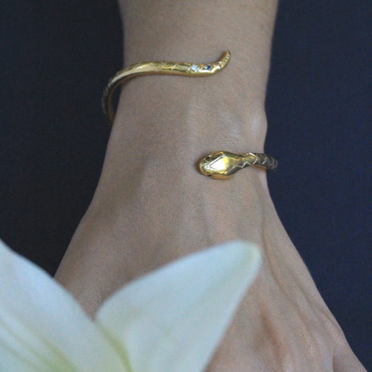 Image is a 24K gold plated snake cuff with garnet eyes, tanzanite and white topaz stones, handmade by Izaskun Zabala.
