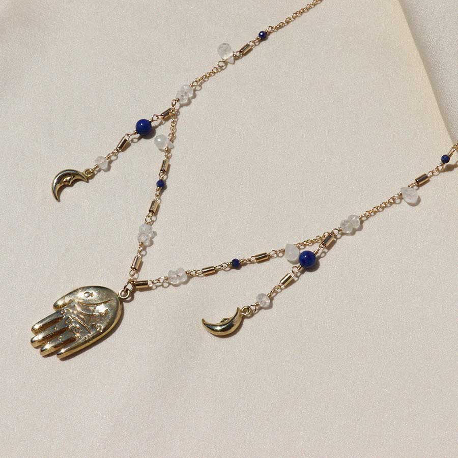 Image is a palmistry hand and moon statement necklace with white sapphire, lapis lazuli and moonstone beads, handmade by Izaskun Zabala.