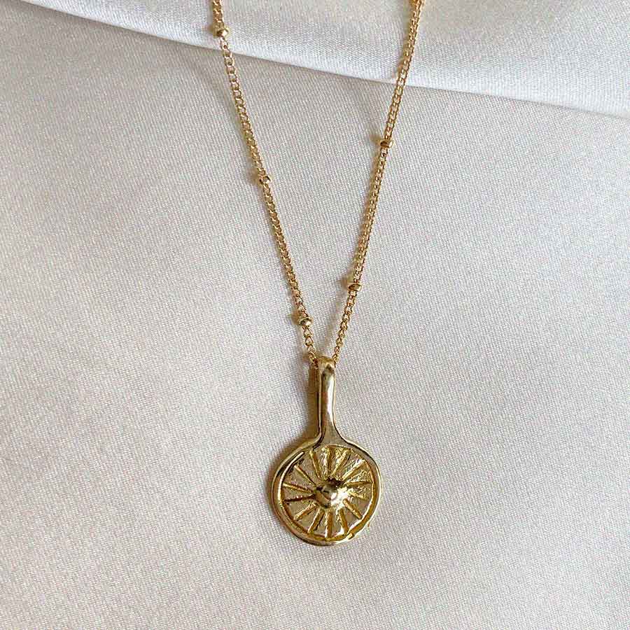 Image is a necklace with a small round brass pendant representing the sun with a gold filled chain handmade by Izaskun Zabala.