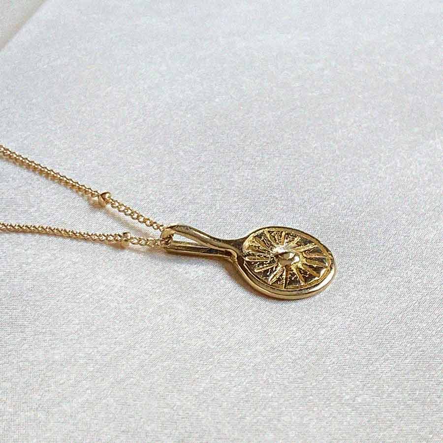 Image is a necklace with a small round brass pendant representing the sun with a gold filled chain handmade by Izaskun Zabala.
