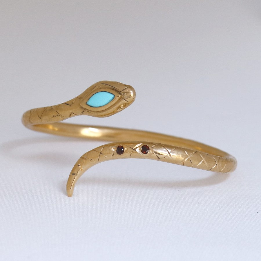 Image is a 24K gold plated snake cuff with turquoise and garnet stones, handmade by Izaskun Zabala.