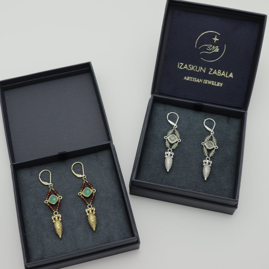 Pair of earrings in a dark blue jewelry boxes with 'Izaskun Zabala Artisan Jewelry' branding.