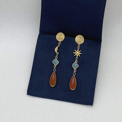 Image is a pair of gold-plated sun and moon with gemstones drop earrings, displayed in the brand's packaging.