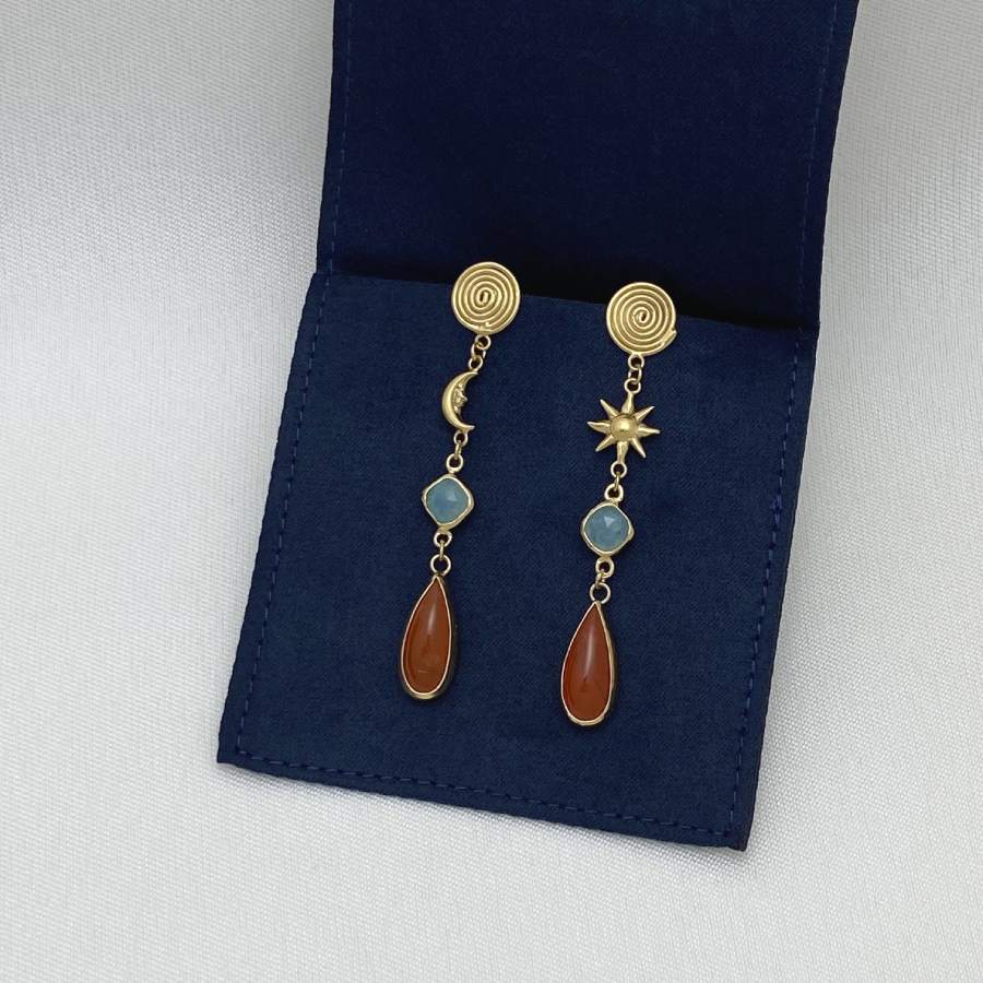 Image is a pair of gold-plated sun and moon with gemstones drop earrings, displayed in the brand's packaging.