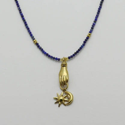 Image is a lapis lazuli beaded chain with a gold-plated miniature hand pendant and removable sun and moon charms, handmade by Izaskun Zabala.