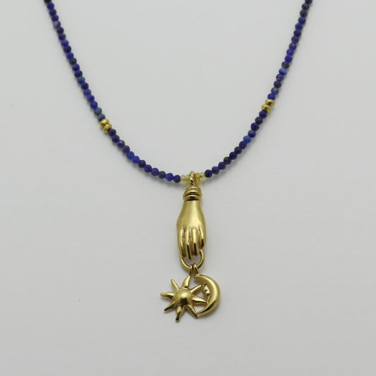 Image is a lapis lazuli beaded chain with a gold-plated miniature hand pendant and removable sun and moon charms, handmade by Izaskun Zabala.