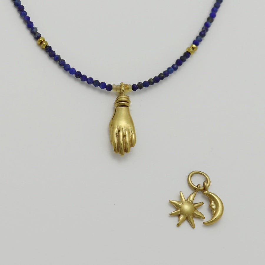 Image is a lapis lazuli beaded chain with a gold-plated miniature hand pendant and removable sun and moon charms, handmade by Izaskun Zabala.