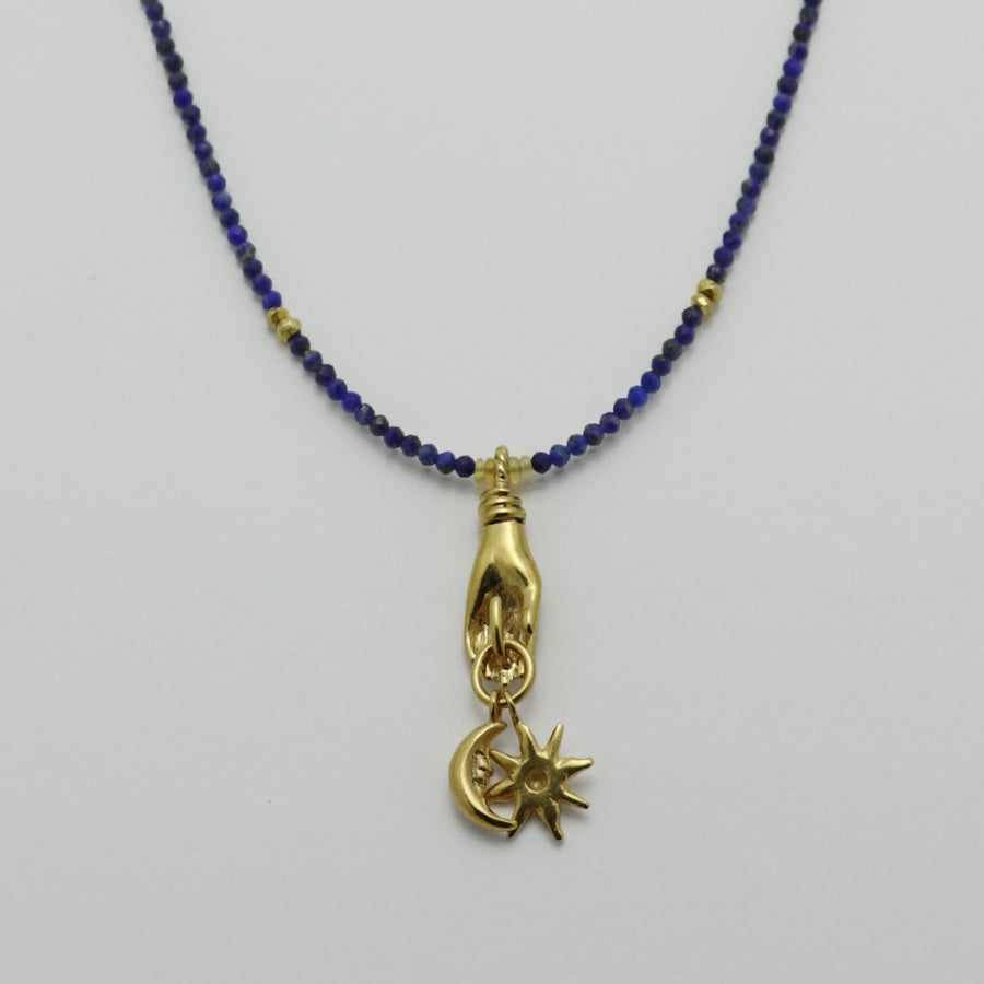 Image is a lapis lazuli beaded chain with a gold-plated miniature hand pendant and removable sun and moon charms, handmade by Izaskun Zabala.