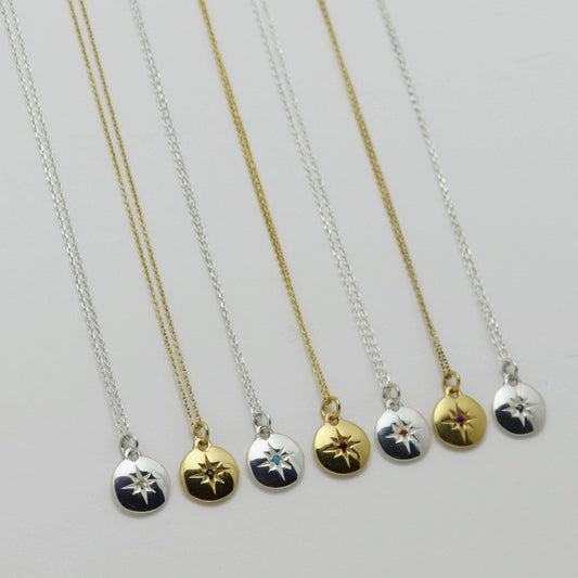 Image is a selection of zodiac necklaces in silver and gold-plate, with a small medallion pendant and star engraved birthstone, handmade by Izaskun Zabala.
