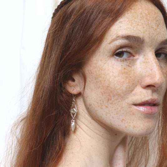 Image is a model wearing silver drop earrings with a carved amphora, a cushion cut amethyst stone and quartz beads, handmade by Izaskun Zabala.