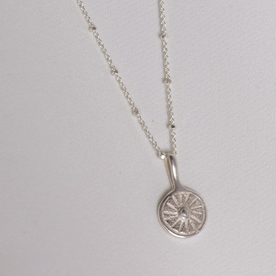 Image is a silver disc pendant necklace representing the sun, handmade by Izaskun Zabala. 