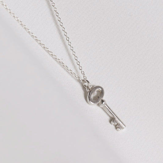 Image is a silver key charm pendant delicate necklace, handmade by Izaskun Zabala.