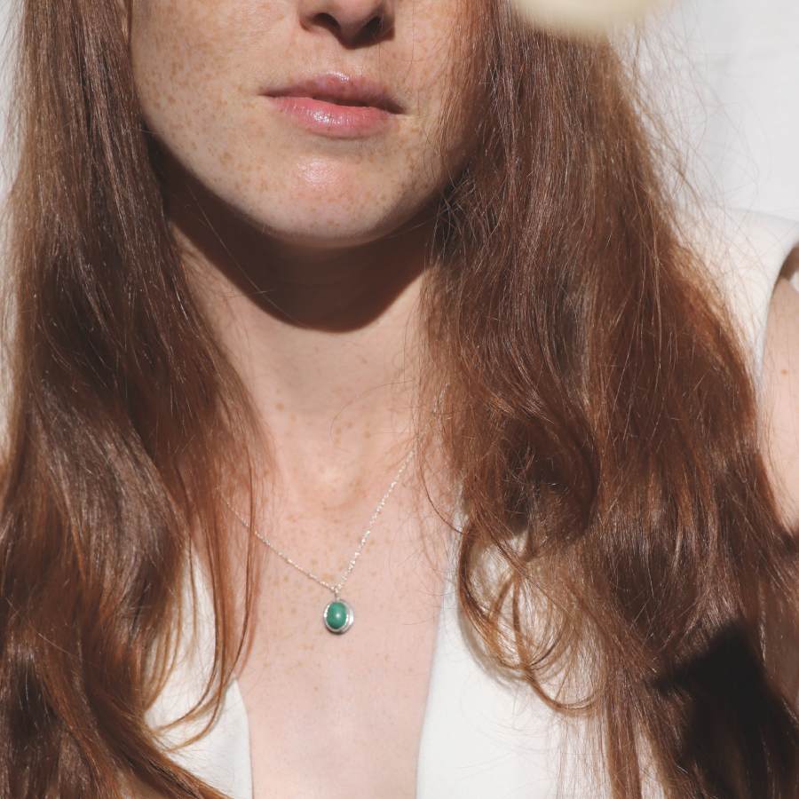 Image is an oval silver pendant with malaquite cabochon and delicate chain on a model, handmade by Izaskun Zabala.