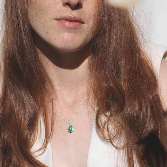 Image is an oval silver pendant with malaquite cabochon and delicate chain on a model, handmade by Izaskun Zabala.