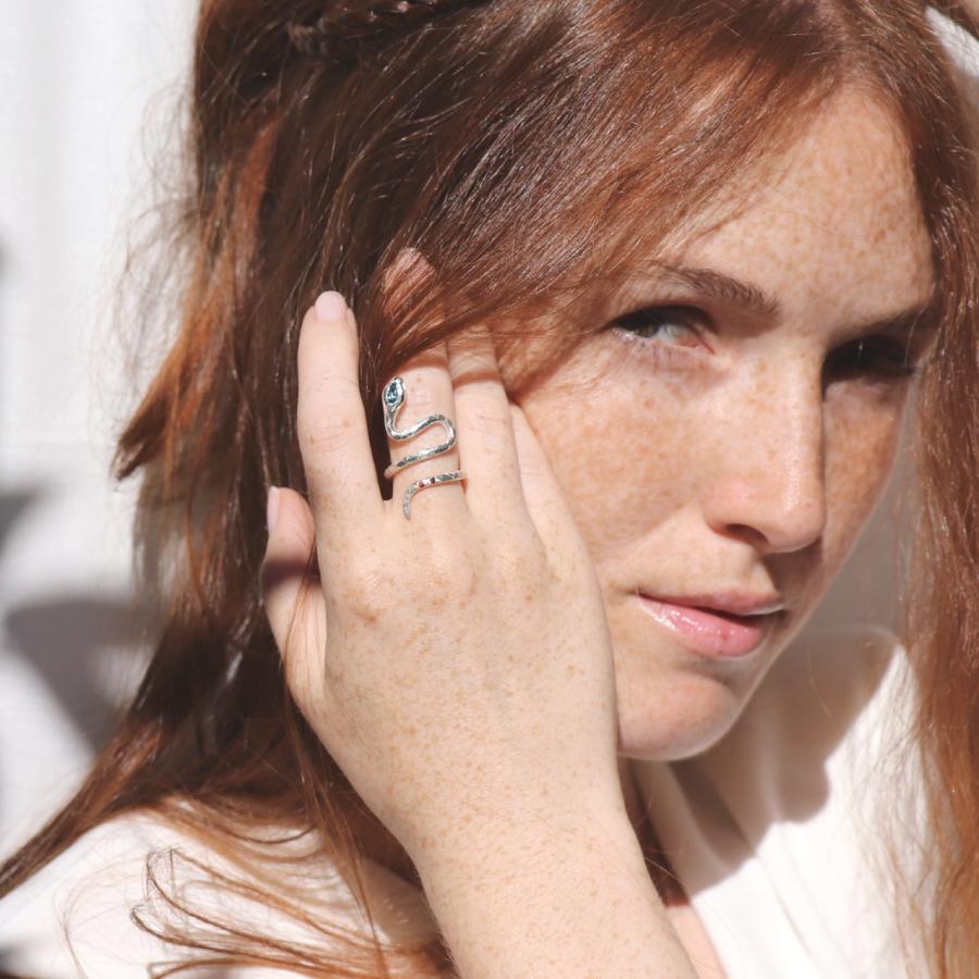 Image is a female model wearing a silver snake ring with a pear shape topaz and two garnets in the tail, handmade by Izaskun Zabala.