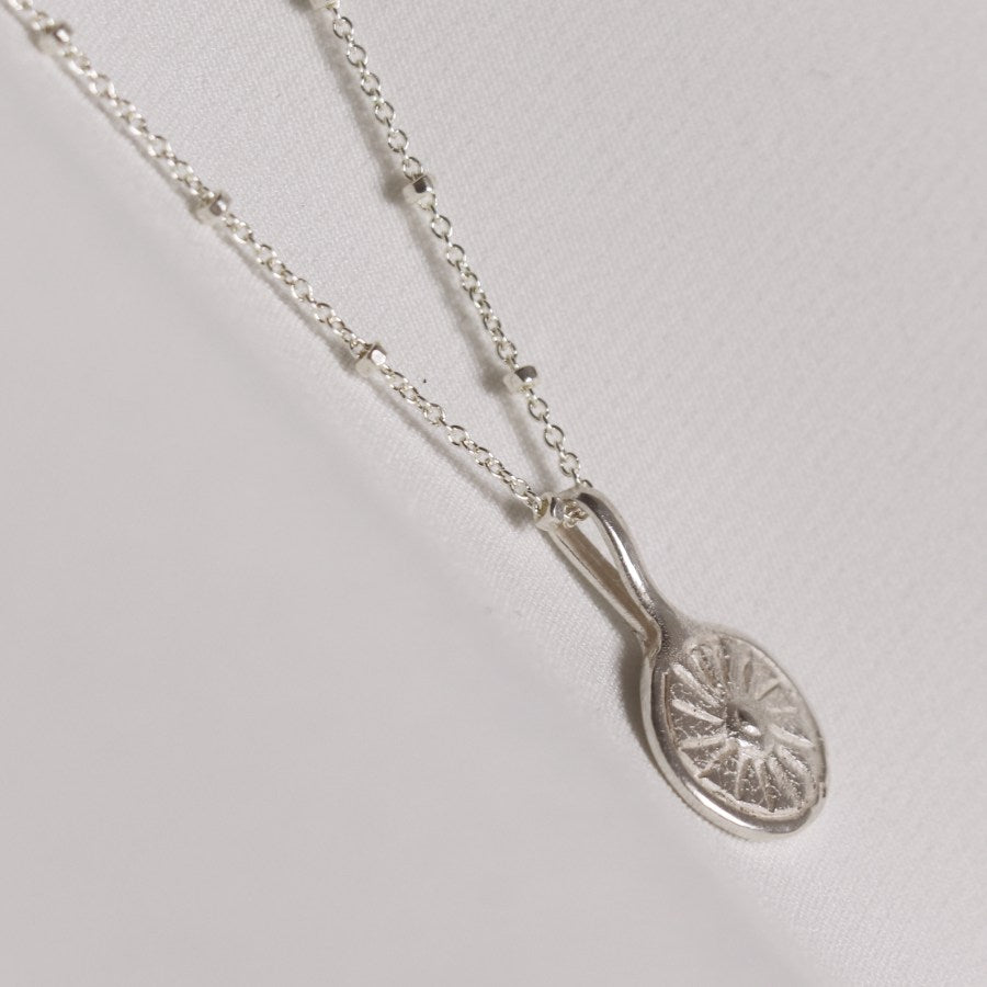 Image is a silver disc pendant necklace representing the sun, handmade by Izaskun Zabala. 