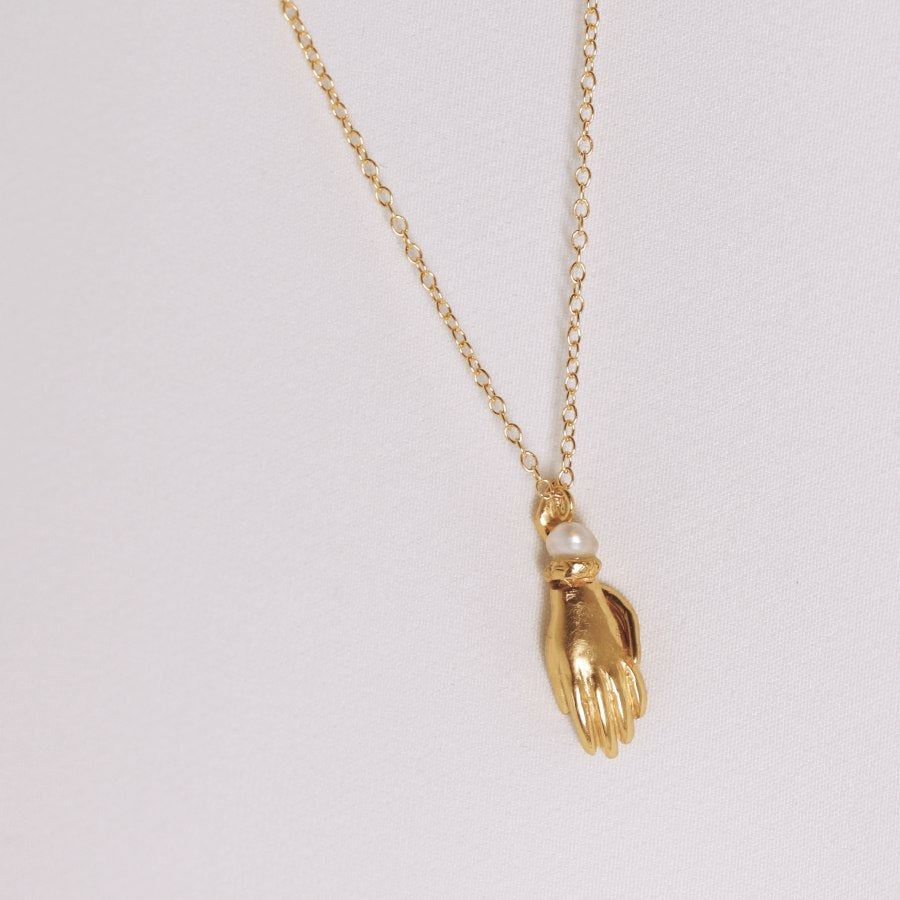 Image is a carved hand and snake pendant with topaz and pearl gold plated necklace, handmade by Izaskun Zabala.