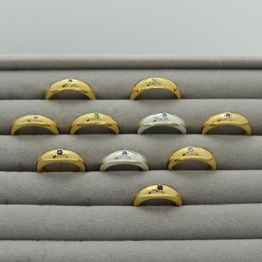 Gold plated and silver rings with an engraved star and gemstones, handmade by Izaskun Zabala, on a gray cushioned display.