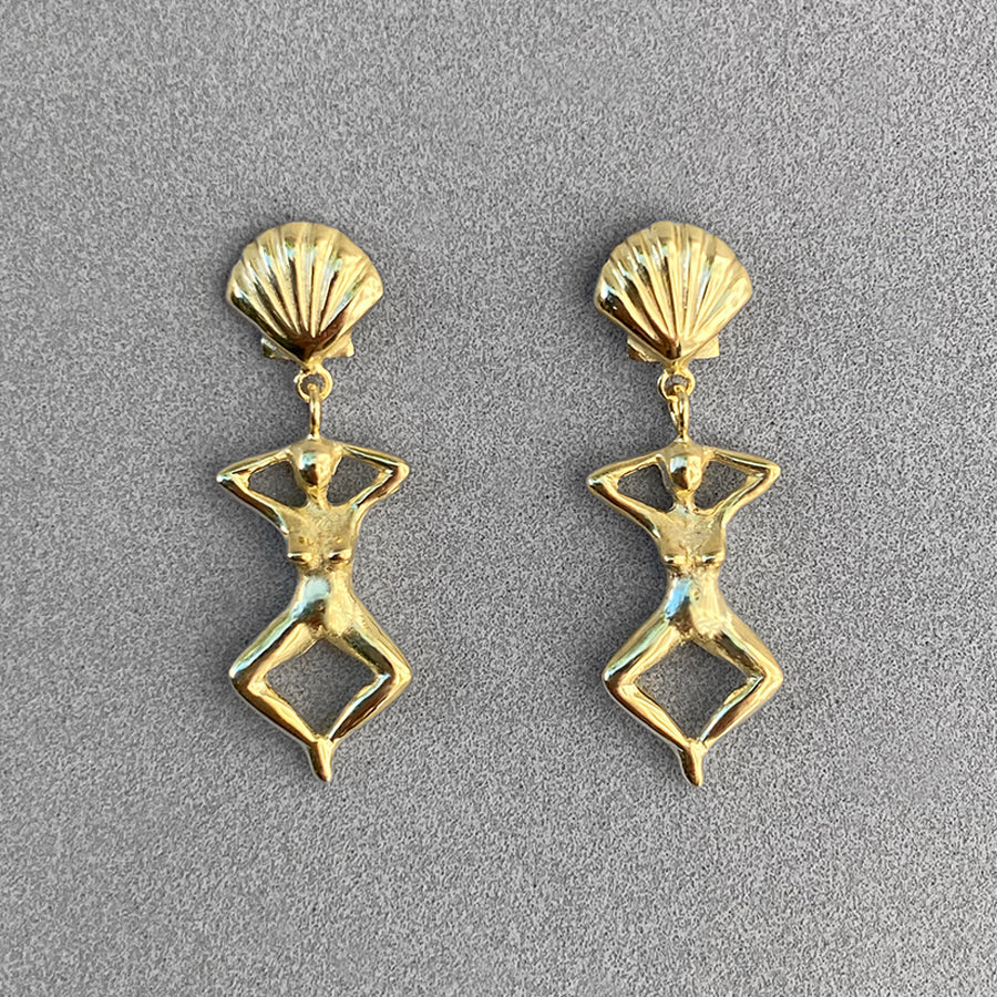 Image is a pair of earrings of a woman&#39;s figure dangling from a shell stud, handmade by Izaskun Zabala.