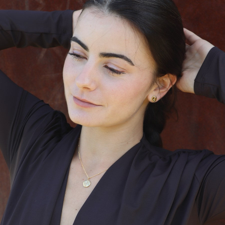 Woman wearing gold-plated yin yang stud earrings and necklace, made by artisan Izaskun Zabala.