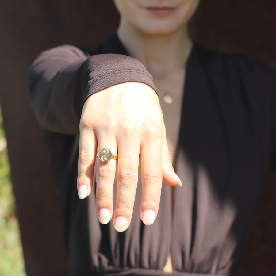 Woman wearing a yin yang gold-plated ring on a blurred outdoor background.