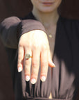 Woman wearing a yin yang gold-plated ring on a blurred outdoor background.