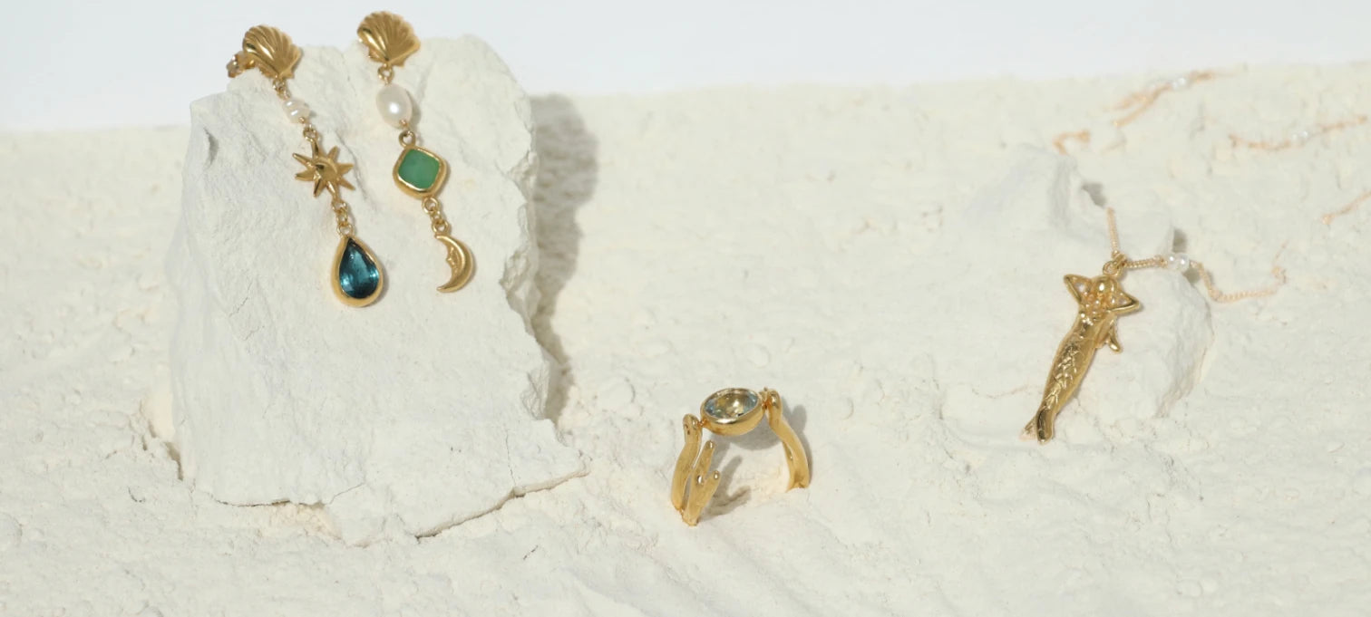 Gold-plated celestial and sea inspired gemstone jewelry on a textured white surface, handmade by Izaskun Zabala