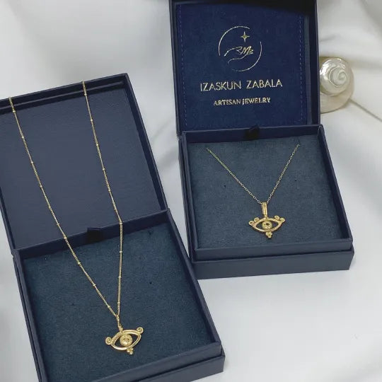 Two handmade eye pendant necklaces on Izaskun Zabala´s branded dark blue packaging boxes.