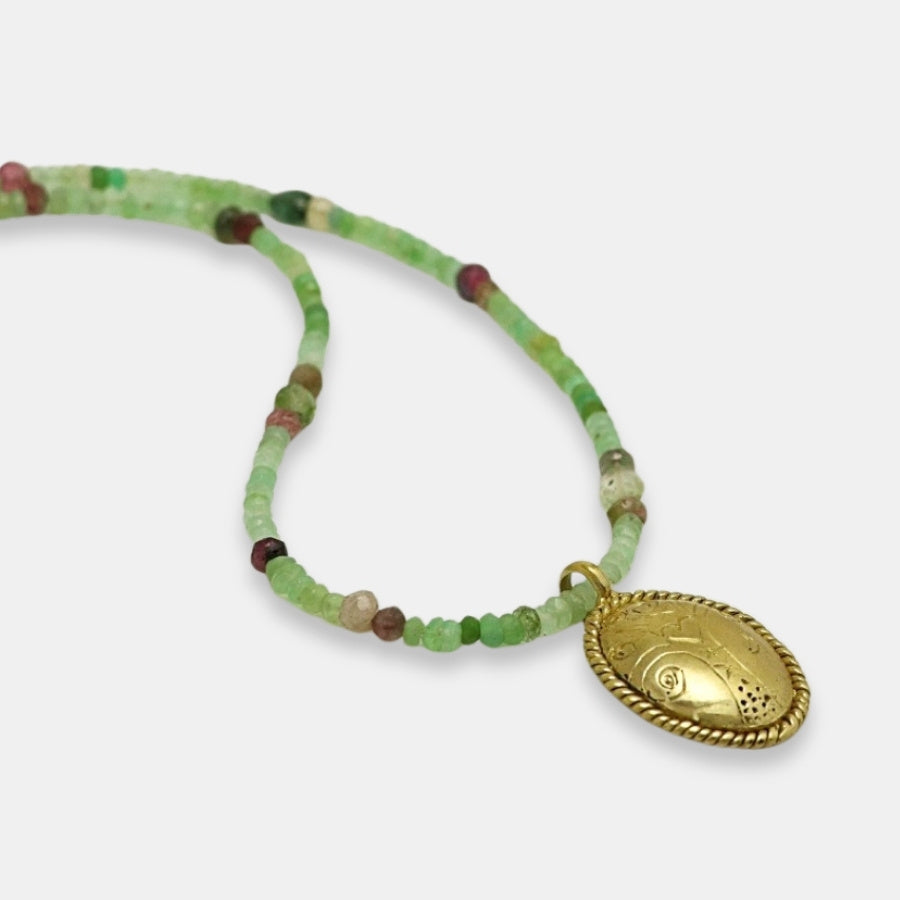 Detail of green and pink gemstone beads necklace with a gold-plated oval engraved medallion, handmade by Izaskun Zabala.