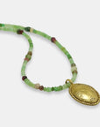 Detail of green and pink gemstone beads necklace with a gold-plated oval engraved medallion, handmade by Izaskun Zabala.