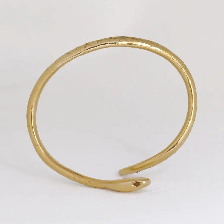 Side view of 24K gold-plated snake-shaped bracelet with garnet eyes, handmade by Izaskun Zabala.