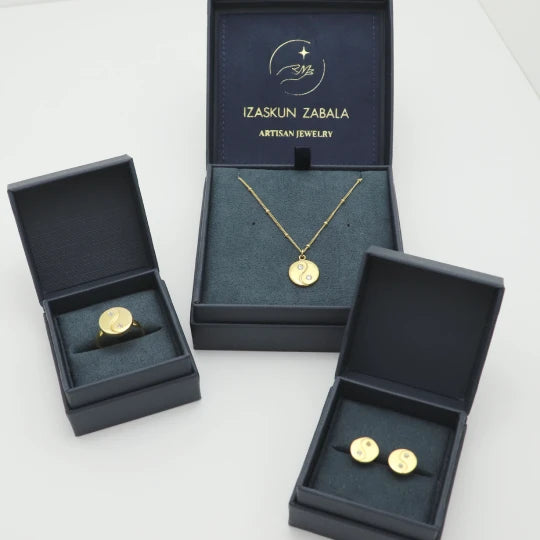 Gold-plated jewelry set including a necklace, ring, and studs in open dark blue boxes with 'Izaskun Zabala Artisan Jewelry' branding.
