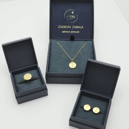 Gold-plated jewelry set including a necklace, ring, and earrings in open dark blue boxes with 'Izaskun Zabala Artisan Jewelry' branding.