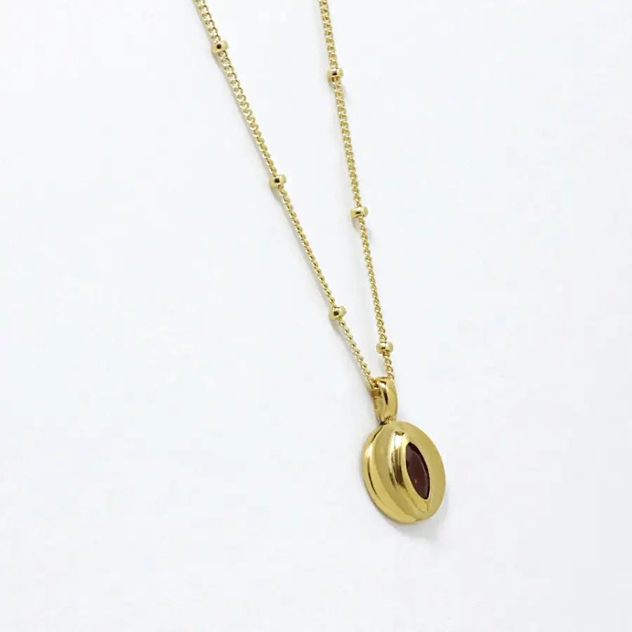 Side view of 24K gold-plated small disk pendant with garnet marquise delicate necklace, handmade by Izaskun Zabala.