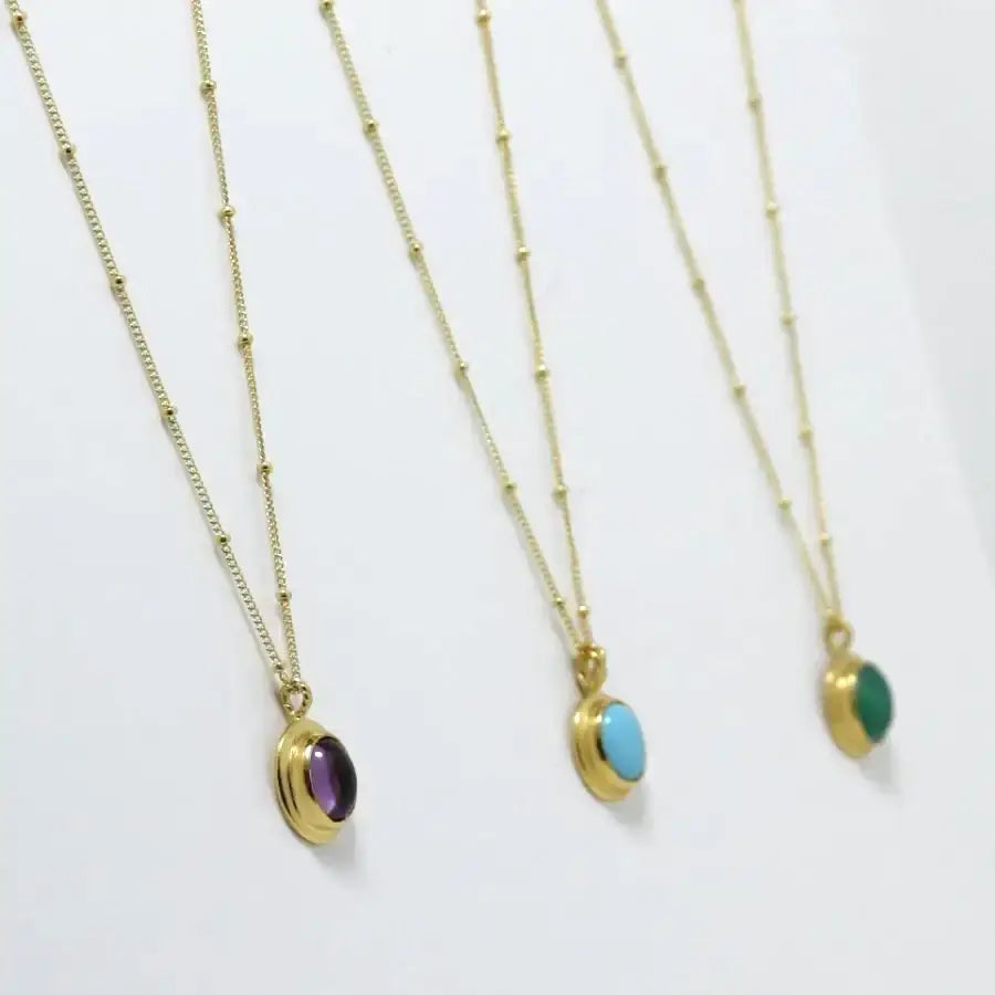 Side view of three gold-plated oval cabochon pendant necklaces, handmade by Izaskun Zabala.