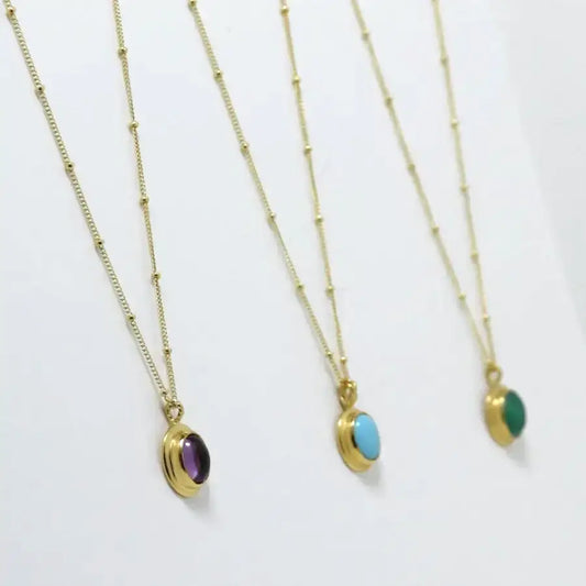 Side view of three gold-plated oval cabochon pendant necklaces, handmade by Izaskun Zabala.
