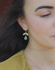 Close-up of a woman wearing gold-plated leaf earrings with green teardrop stone.