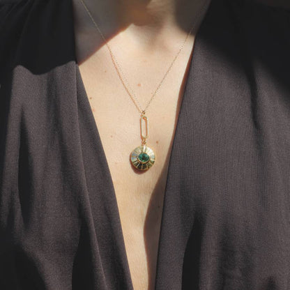 Gold-plated necklace with a green pendulum pendant on a woman wearing a dark brown top.