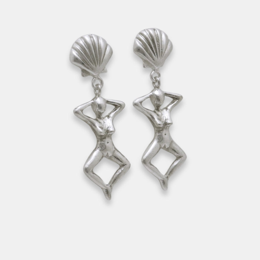Side view of silver earrings with shell-like tops and female figure dangles, handmade by Izaskun Zabala.