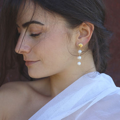Close-up of a woman wearing golden shell stud and pearl drop earrings.