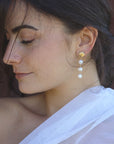 Close-up of a woman wearing golden shell stud and pearl drop earrings.