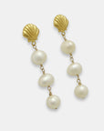 Side view of a pair of gold-plated earrings with shell studs and pearl drops on a white background.